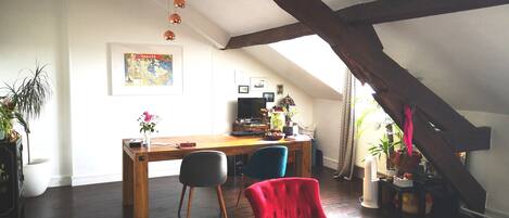 Una habitación cálida en el ático con un escritorio de madera, dos sillas, un sillón rojo y un mapa en la pared.