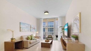 A modern living room with a sofa, coffee table, and TV stand, large windows, and artwork on the walls. - Perfect Relax| Rooftop Pool – Hot Tub+Gym (Hollywood)