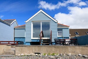 A coastal building with a large sliding glass door, a small patio with outdoor furniture, and a clear view of the sky. - Beach Side House in Beautiful Borth (Borth)