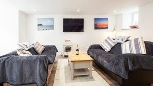 A modern living room with two sofas, a coffee table, and a fireplace. There are three framed pictures on the wall and a small shelf with decorative items. - Beach Side House in Beautiful Borth (Borth)
