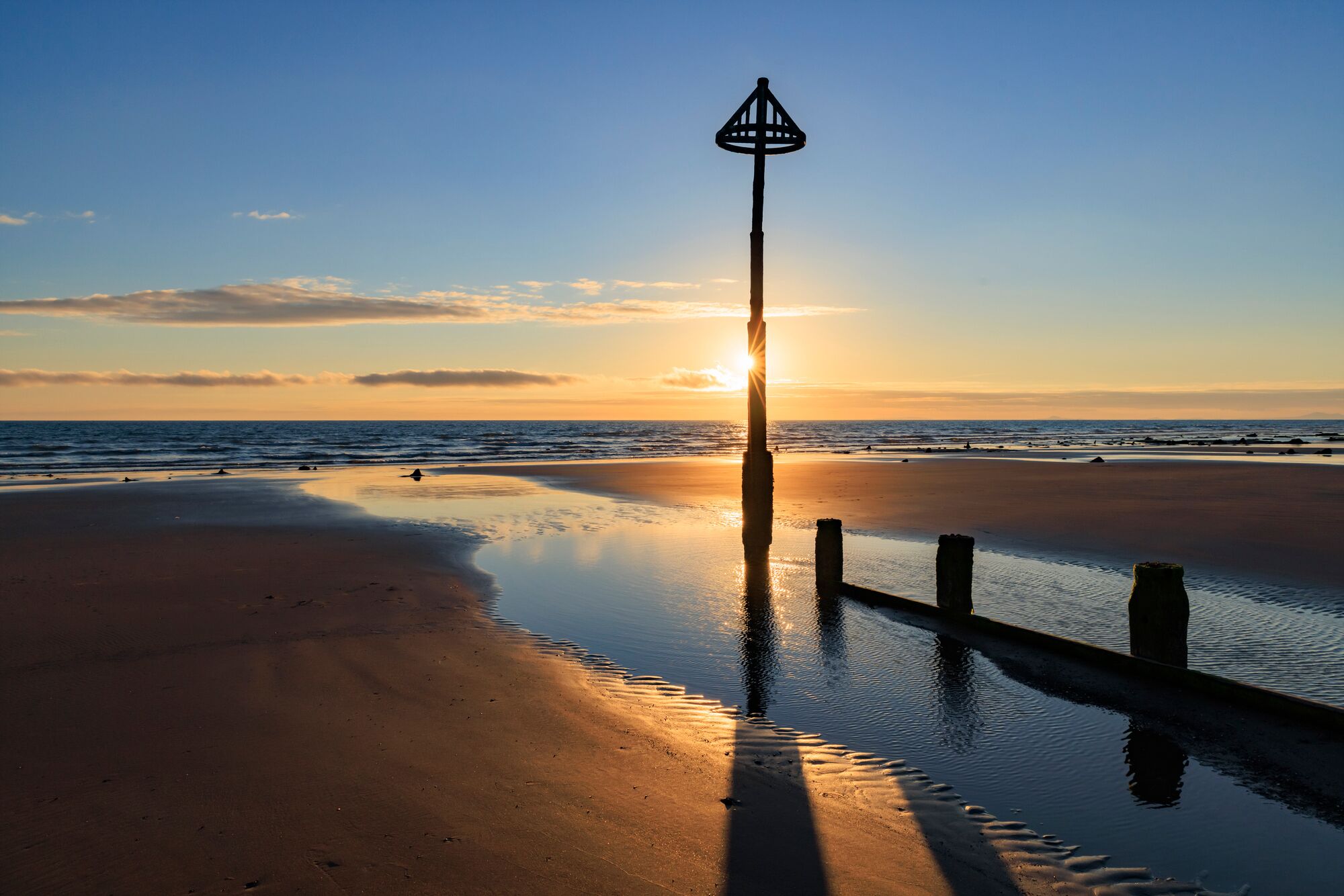 A beach scene with a solitary lamp post and calm waters reflecting the sunset.