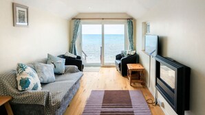 A cozy living room with a sofa, a television, and a view of the sea through large windows. - Beach Side House in Beautiful Borth (Borth)