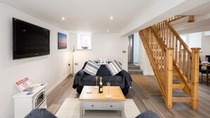 A modern living room with a sofa, a coffee table, a TV, and a wooden staircase. - Beach Side House in Beautiful Borth (Borth)