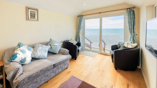 A cozy living room with a sofa, two armchairs, a wooden floor, and a large window offering a view of the beach. - Beach Side House in Beautiful Borth (Borth)