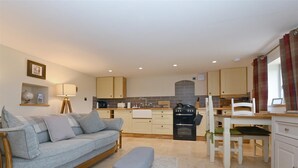 A compact living space with a sofa, a dining table, a kitchen area with a stove, and a small bench.