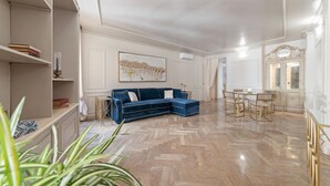 Een ruime woonkamer met een blauwe modulaire bank, een vloer met een herringbone-patroon, een eethoek met een tafel en stoelen, en een groot schilderij aan de muur.