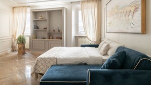 Een slaapkamer met een bed, een blauwe bank, een kledingkast en een groot abstract schilderij aan de muur.