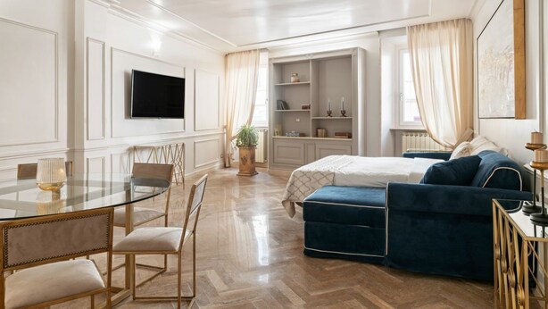 Hotelkamer met een rond glazen tafeltje, een bed met een blauw gestoffeerd hoofdeinde, een aan de muur bevestigde televisie en een inbouwkast.