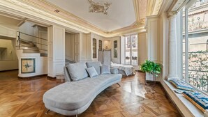 Un salon spacieux avec un canapé gris aux lignes courbes, un escalier et une grande fenêtre offrant une vue dégagée.