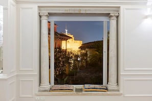 A window with a view of a building at dusk, framed by white columns, and two pillows on the windowsill.