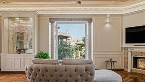 Un salon avec un canapé capitonné, un téléviseur, une cheminée et une vue dégagée sur l’extérieur grâce à une grande fenêtre.