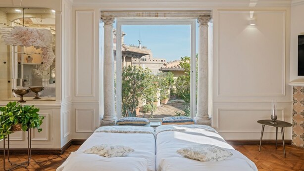 Une chambre avec un grand lit, une vue par la fenêtre, une petite table et une plante décorative.