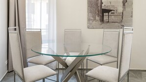 A dining area with a glass table surrounded by four upholstered chairs.