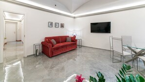 A spacious room with a red sofa, a glass table, and a TV mounted on the wall.