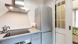 A kitchen with a stainless steel range hood, a refrigerator, a stove, and a door with a frosted glass panel.