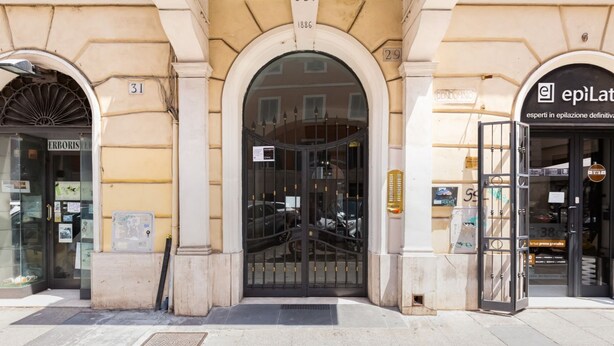 Entrada de un edificio con una verja negra, un letrero que dice 'SBI 1886' y un escaparate con el rótulo 'epiLat'.