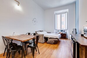 A compact room with a bed, a dining table with chairs, a small kitchenette, and a window.