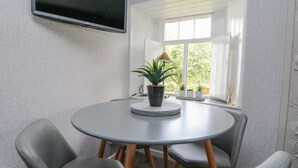 Ein Zimmer mit einem runden Tisch, vier grauen Stühlen, einem flachbildfernseher an der Wand und einem Fenster mit weißen Jalousien.