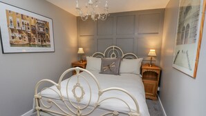 Ein ordentlich eingerichtetes Schlafzimmer mit einem weißen Metallbett, zwei Nachttischen mit Lampen, einer Kristallleuchtre und gerahmten Kunstwerken an den Wänden.