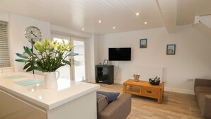 Una sala de estar moderna con una isla blanca, un sofá, un televisor y una mesa de centro de madera.