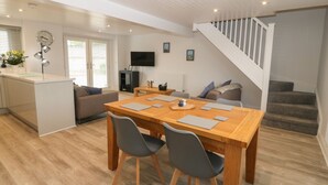 Una cocina moderna con una isla central, una zona de comedor con una mesa y sillas de madera, un sofá y una escalera que conduce a un nivel superior.