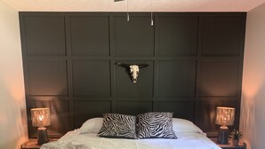 Un dormitorio con una cama grande, almohadas estampadas con motivos de cebra, una decoración de calavera y dos lámparas de noche.