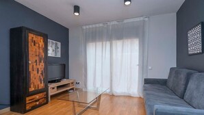 Un salon moderne avec une table basse en verre, un canapé gris, un meuble en bois et un téléviseur posé sur un meuble en bois.
