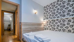 Une chambre d’hôtel avec une tête de lit en bois, un lit recouvert de draps blancs et un mur orné d’un motif floral.