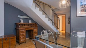 Un escalier avec un bureau et des chaises en bois, une balustrade en verre et une suspension lumineuse.