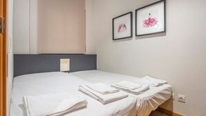 A single bed with white linens and towels, a gray headboard, and two framed pictures on the wall. - Eixample 2 bedroom with private terrace (Barcelona)