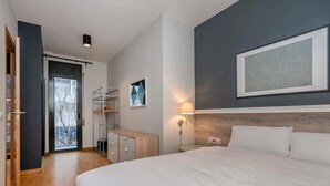 Un dormitorio moderno con una cama grande, un armario, un escritorio y una puerta que da a un balcón.