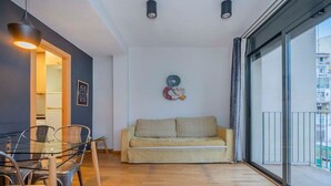 A modern living room with a glass dining table, a beige sofa, and a large window with a view of buildings. - Plaza España 2 bedroom with balcony (Barcelona)