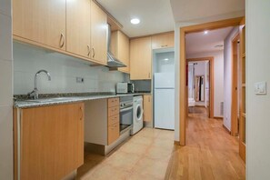 A kitchen with wooden cabinets, a washing machine, and a microwave. - Heart of Eixample 2BD with balcony (Barcelona)