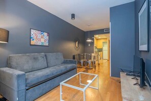 A modern living room with a grey sofa, a glass coffee table, and a dining area with chairs and a table. - Heart of Eixample 2BD with balcony (Barcelona)
