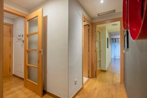 Un couloir doté d’un plancher en bois, une porte avec des panneaux en verre dépoli et un objet rouge accroché au mur.