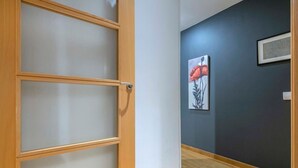 A hallway with a wooden door with frosted glass panels, a dark wall with a framed artwork, and a wooden floor.