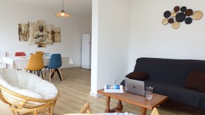 A modern living room with a sofa, a dining table with chairs, and a wall-mounted art piece.