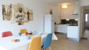 A modern dining area with a table set for two, a kitchen in the background, and artwork on the wall.