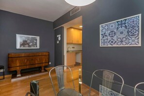 A modern interior with a wooden bench, metal chairs, a dining table, a kitchen area, and a decorative tile wall.