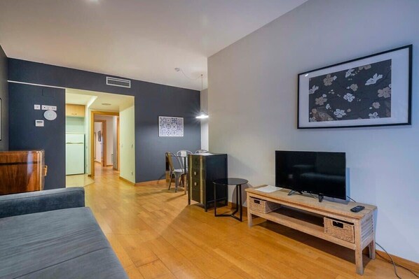 A modern living room with a flat-screen TV, a sofa, a dining table, and chairs.