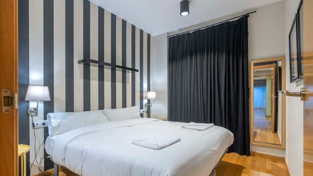 Une chambre d’hôtel avec un lit, des lampes de chevet, un miroir et un rideau noir.