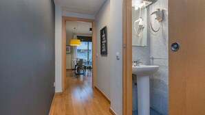 Un pasillo con piso de madera que conduce a un baño con lavamanos blanco y ducha.