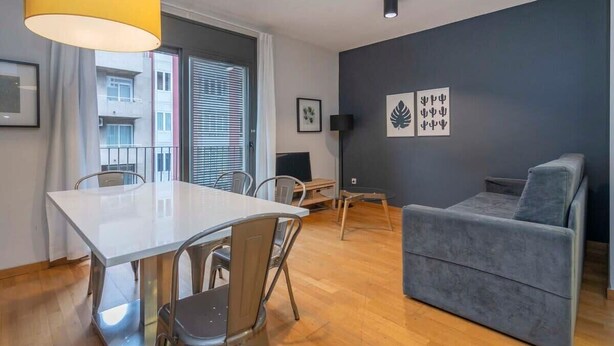 Una sala de estar moderna con comedor, sofá gris y un amplio ventanal con persianas.