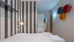 Habitación de hotel con cama, lámpara y pared con diseños a rayas y decoraciones hexagonales.