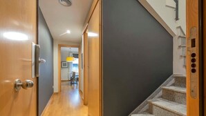 Un pasillo con puertas de madera, una escalera y una zona de cocina al fondo.
