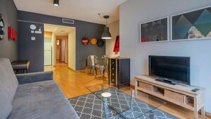 Un salon moderne avec un canapé gris, un téléviseur posé sur un meuble en bois et un coin repas comprenant des chaises et une table.