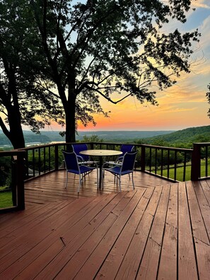 A wooden deck with a table and chairs, surrounded by trees and a scenic view.