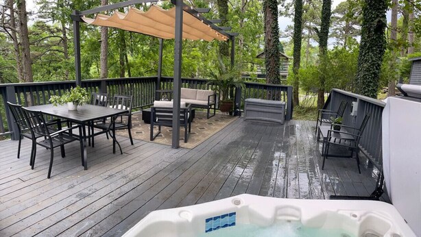 Una terraza de madera con mobiliario exterior, un jacuzzi y una pérgola.