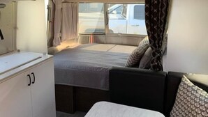 A compact RV interior with a bed, kitchenette, and a small seating area.