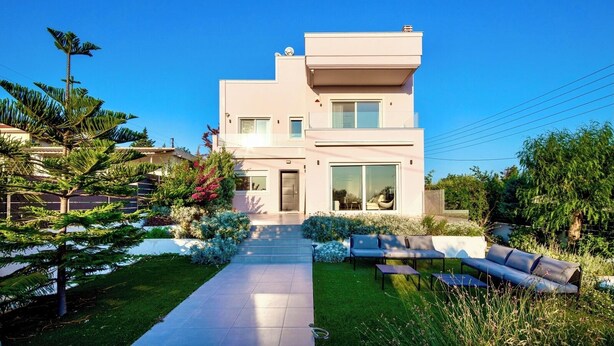 A modern two-story house with a flat roof, large windows, and a well-maintained garden with a pathway leading to the entrance. - 2 Coastal villas 5 min. From beach. Panoramic view of sea and sunset (Καλύβια Θορικου)